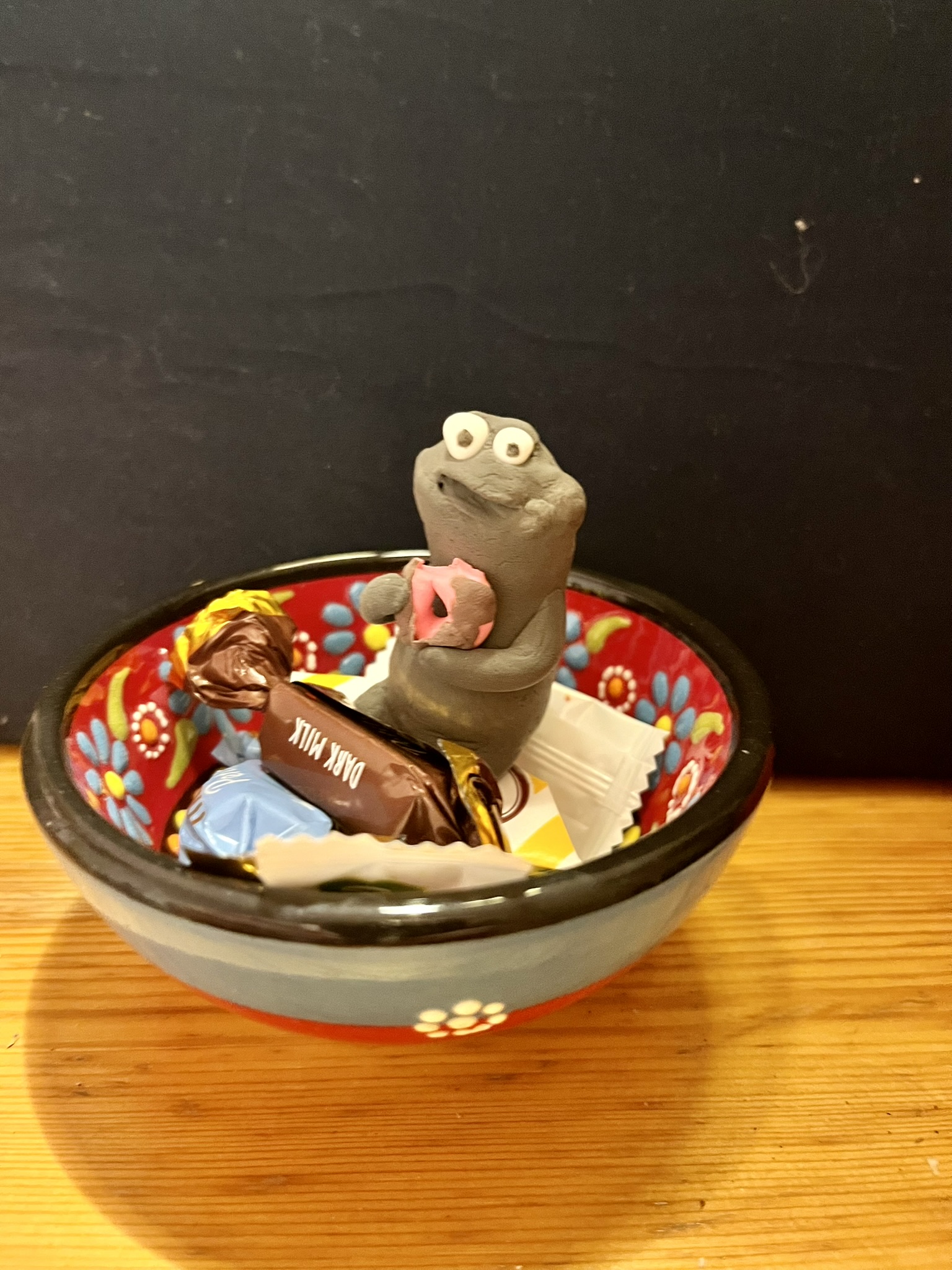 Grauer Squig mit rosa Donut in Schale voller Pralinen